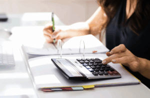 Personne effectuant des calculs budgétaires sur une calculatrice et des documents comptables. Norme 18 - M57